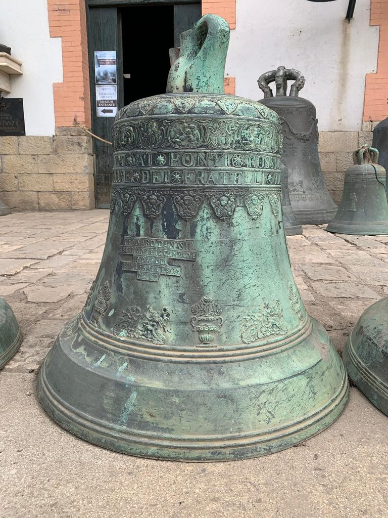 Primo piano di una campana in bronzo decorata esposta all’ingresso della fonderia Marinelli